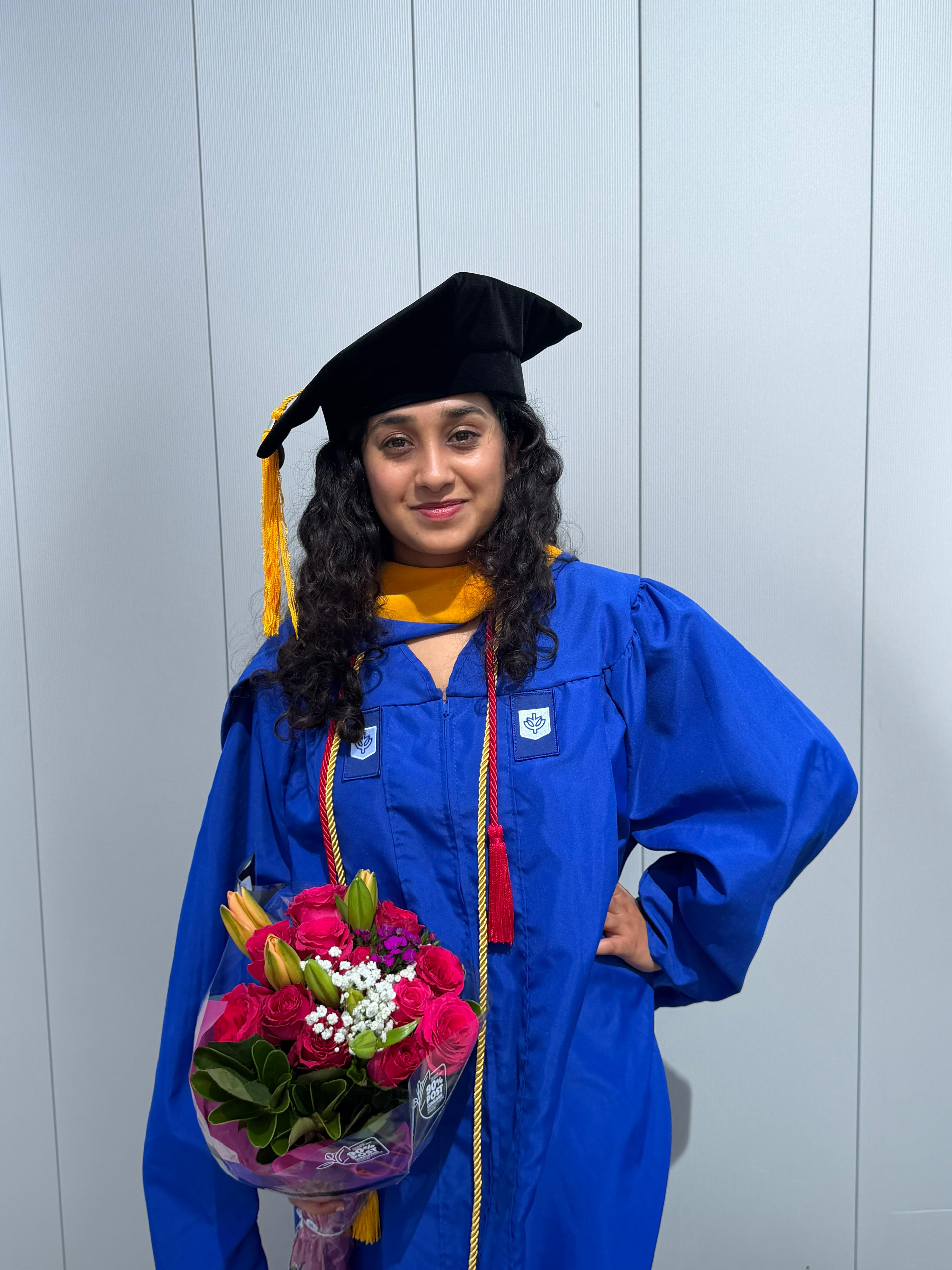 Anusha Prasad at her DePaul graduation, wearing a cap and gown and holding a bouquet
