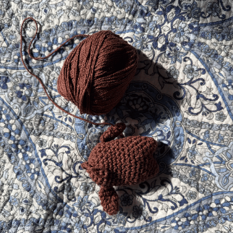 A crocheted bunny beside a ball of brown yarn