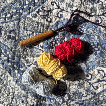 Crochet hook and mini yarn balls on a quilt