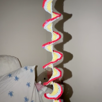 A crocheted spiral wind spinner hanging by the bed